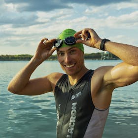 Confident male athlete adjusting goggles at a lake during a sunny day, ready for training.