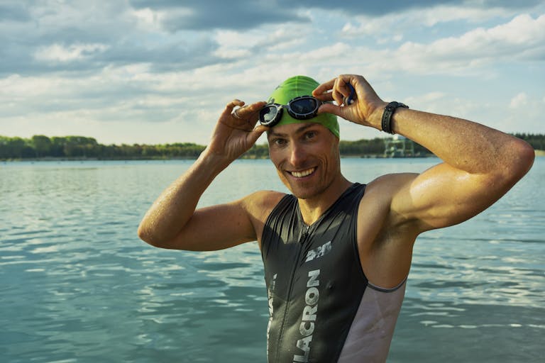 Confident male athlete adjusting goggles at a lake during a sunny day, ready for training.