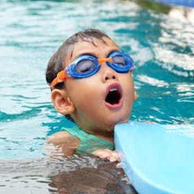 Young child swimming in a pool wearing blue goggles, enjoying summer.