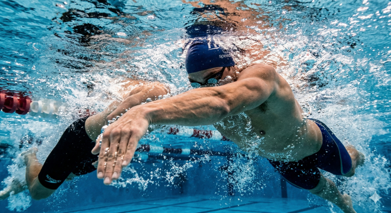 A hyper-realistic underwater shot focusing on a swimmer's hand and forearm in the "High-Elbow Catch" position. The water is churning with power, and the muscles in the arm are clearly defined. 8k, cinematic sports lighting